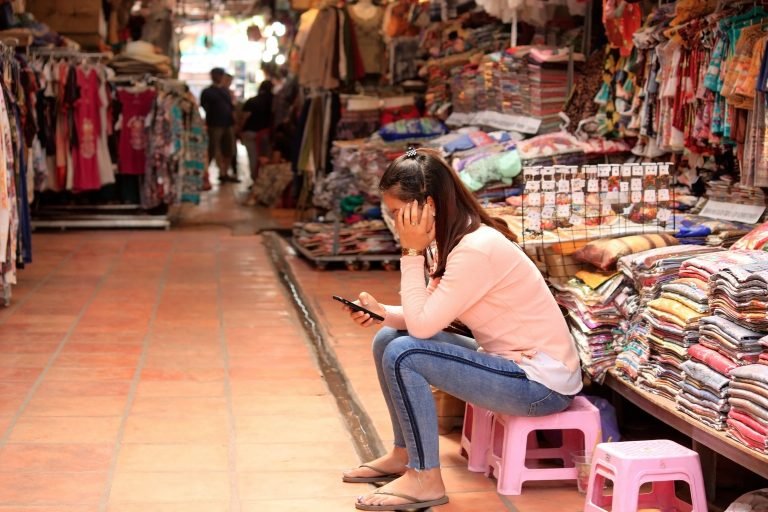 Local vendor sitting at a market stall in Siem Reap surrounded by clothing and handmade goods