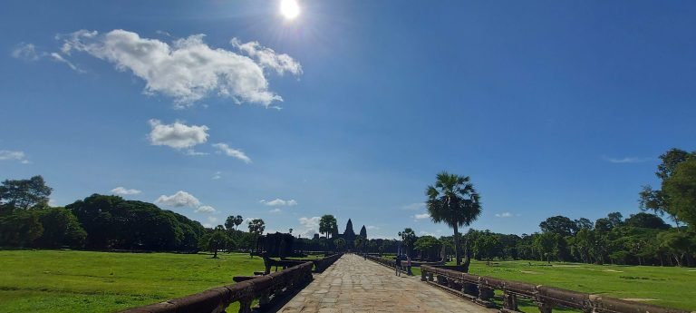 Angkor Wat Guide showing long stone causeway leading toward temple with palm trees and bright sky in Siem Reap Cambodia