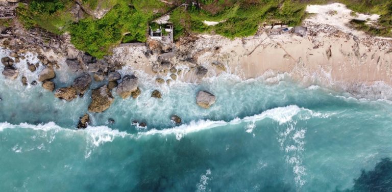 Aerial view of turquoise ocean waves meeting a rugged Bali shoreline, showcasing Bali travel tips for exploring the island's diverse coastal landscapes Caption: Description:
