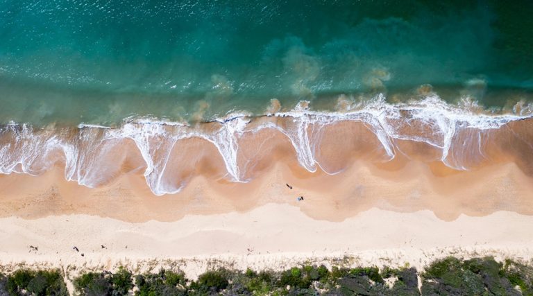 Aerial view of waves meeting golden sand along one of the beautiful beaches in Sydney