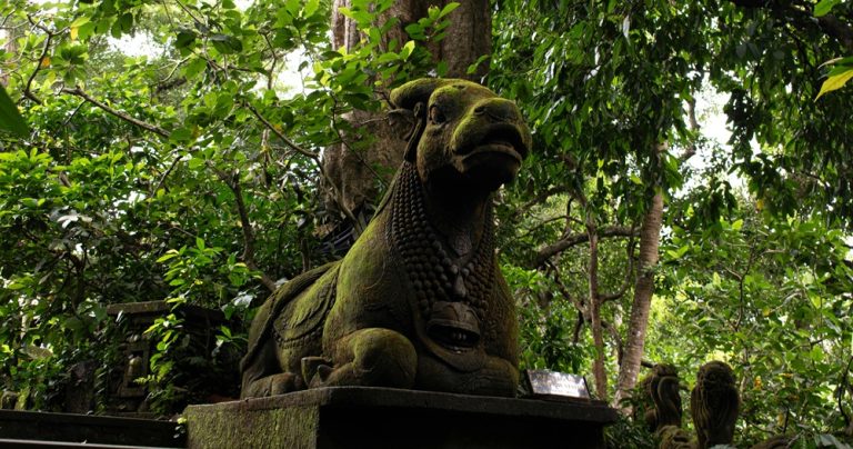Ancient moss-covered guardian statue surrounded by lush tropical jungle in Ubud, Bali