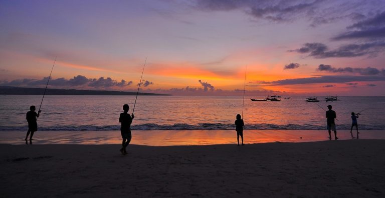 Fishermen standing on a Bali beach at sunset with traditional boats offshore, illustrating Bali travel tips for experiencing local culture and coastal life