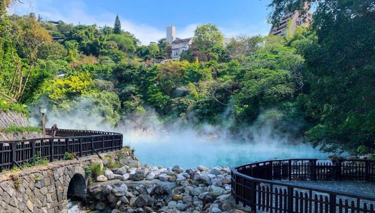 Taiwan hot springs at Beitou Geothermal Valley with steaming blue geothermal water, stone walkways, and lush green hillside scenery