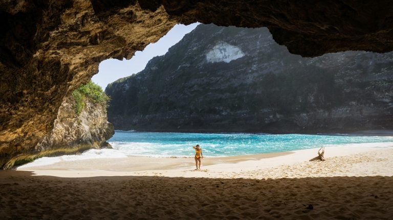 Hidden cave opening overlooking turquoise water and white sand at Kelingking Beach in Bali beaches on Nusa Penida