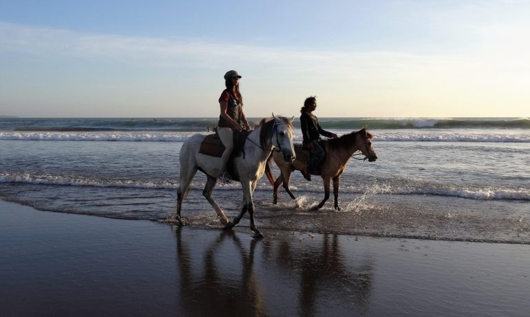 Travelers horseback riding along a Bali beach at sunset, showcasing coastal experiences accessible when learning how to get around Bali Caption: Description: