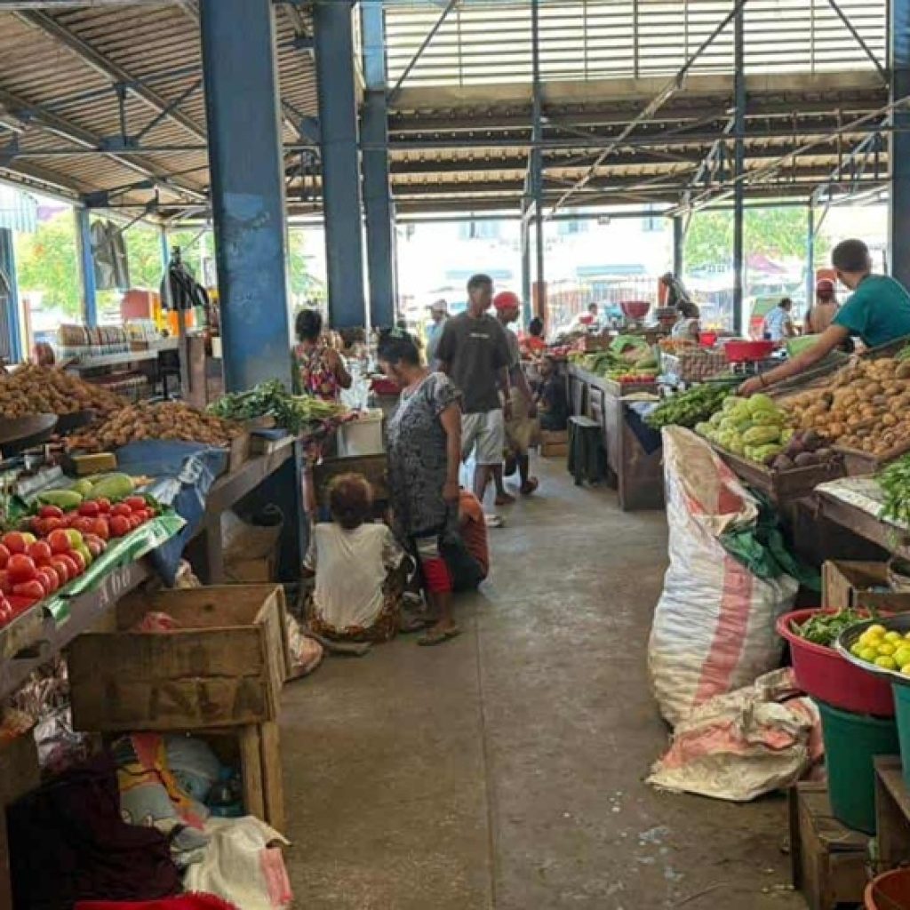 Marché couvert malgache avec étals de légumes, fruits frais et habitants faisant leurs courses