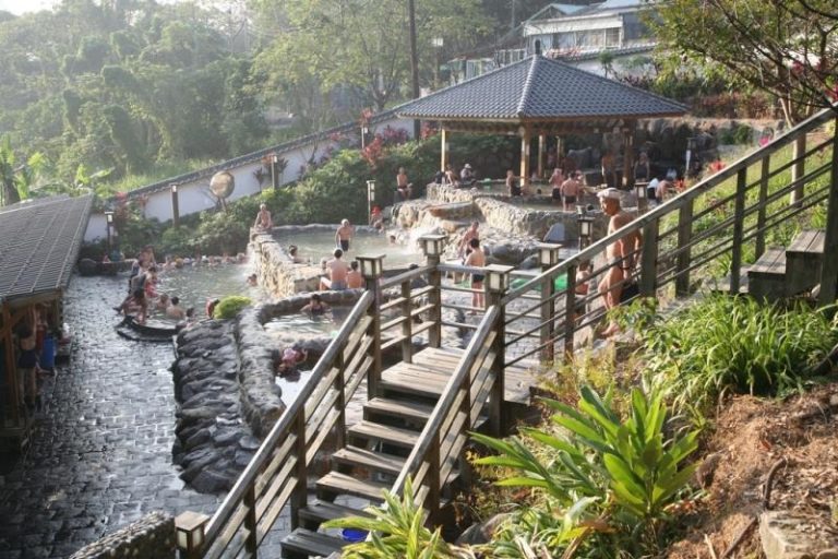 Taiwan hot springs with outdoor geothermal bathing pools, traditional pavilion, stone terraces, and mountain onsen atmosphere Caption: Description: