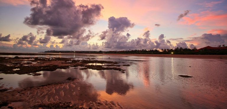 Pink sunset reflecting across shallow ocean water and tropical coastline in Bali