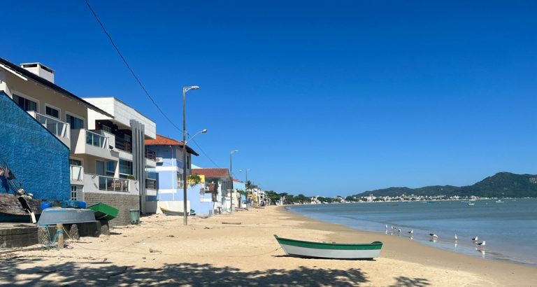 Quiet sandy shoreline with small fishing boats and residential homes along the coast near Florianópolis