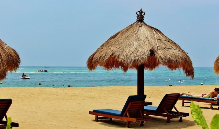 Beach loungers and thatched umbrellas along the sandy beach in Nusa Dua, Bali