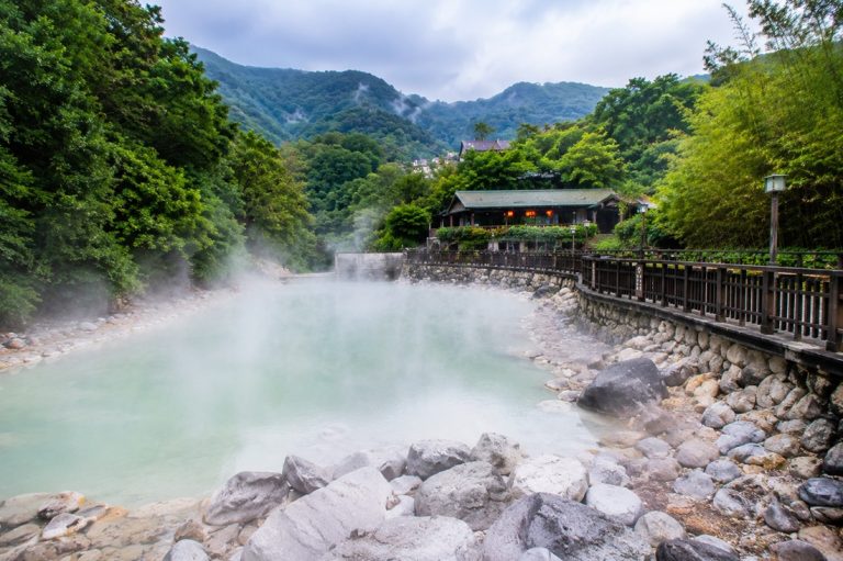 Taiwan hot springs with steaming geothermal river pools, stone walkways, forested mountains, and traditional onsen atmosphere Caption: Description: