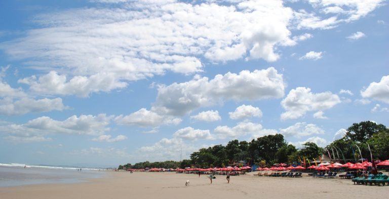 Wide sandy coastline and beach umbrellas along Seminyak Beach in Bali beaches under a bright tropical sky Caption: Description: