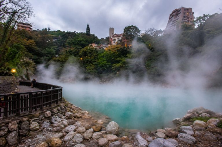 Taiwan hot springs at Beitou with steaming turquoise geothermal water, wooden walkway, rocks, and misty hillside scenery in Taipei