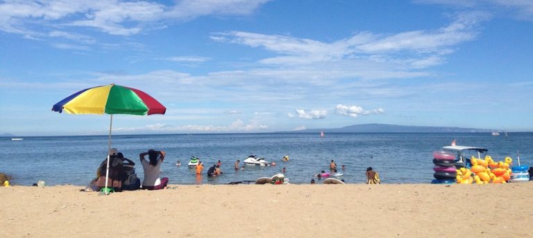 Travelers relaxing on a sunny beach with calm ocean water and colorful umbrellas in Bali
