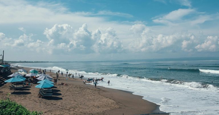 Beach umbrellas and surfers along the coastline in Canggu, Bali Caption: Description: