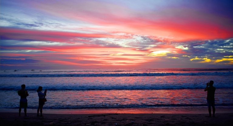 Colorful sunset at Kuta Beach with visitors watching the ocean, showcasing how to get around Bali and explore its famous coastal destinations