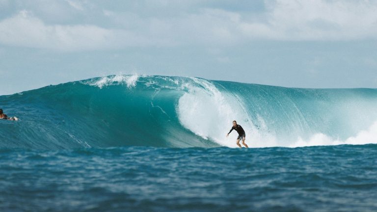 Surfer riding a large turquoise wave near the coastline of Nusa Penida during strong ocean conditions