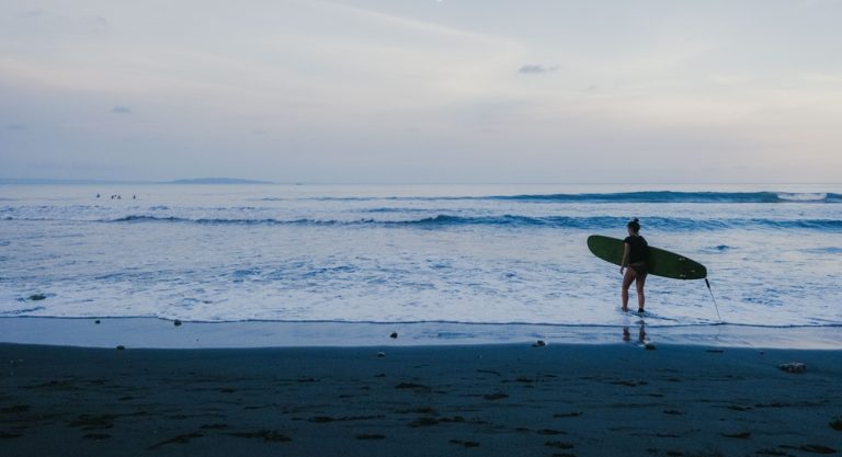 Surfer walking into the waves at Balian Beach in Bali beaches during a calm evening on the west coast