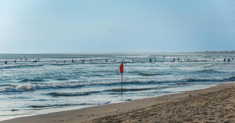 Surfers riding waves along Legian Beach in Bali beaches during a sunny afternoon on the island’s southwest coast
