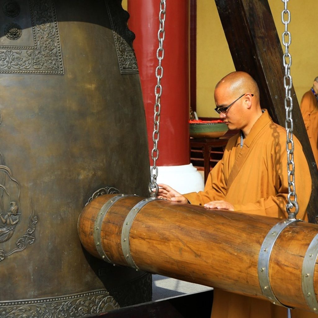 Taiwan Travel Budget Guide: Exploring Taiwan’s Temples Without Overspending Alt Text: Monk striking a large temple bell in Taiwan during a cultural ceremony - Taiwan travel budget guide