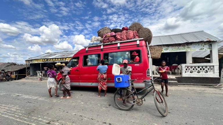 Taxi-brousse rouge transportant passagers et marchandises dans une ville de Madagascar