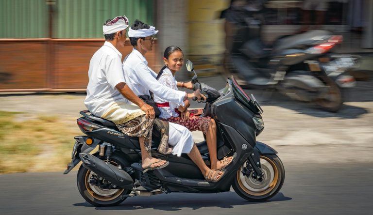 Traditional Balinese family riding a scooter through a village street in Bali, Indonesia Caption: Description:
