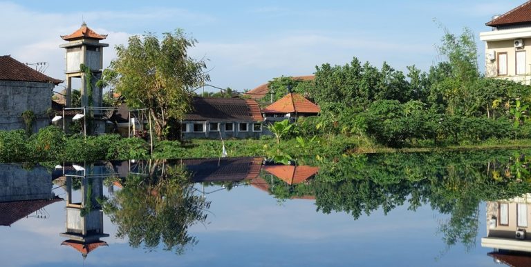 Traditional Balinese village reflected in calm water surrounded by tropical greenery in Bali Caption: Description: