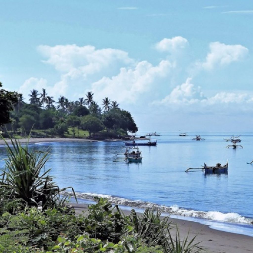 Traditional fishing boats anchored along the calm coastline in East Bali beaches with tropical scenery and volcanic black sand