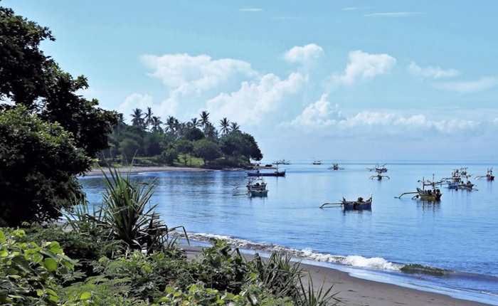 Traditional fishing boats anchored along the calm coastline in East Bali beaches with tropical scenery and volcanic black sand