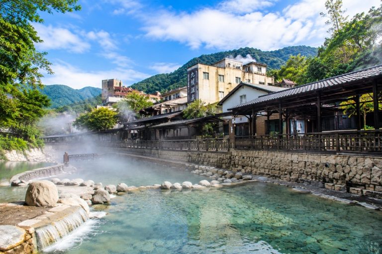Taiwan hot springs in a traditional mountain town with steaming geothermal water, stone river pools, and wooden onsen buildings Caption: Description: