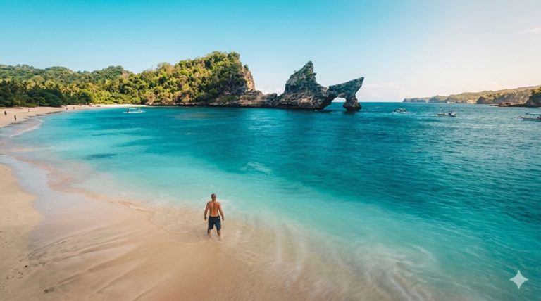 Traveler standing on the shoreline at Atuh Beach with turquoise water and dramatic rock formations in Nusa Penida