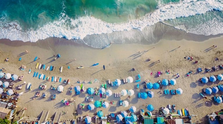 Aerial view of Echo Beach with surfers, beach umbrellas, and waves rolling onto Bali's coastline
