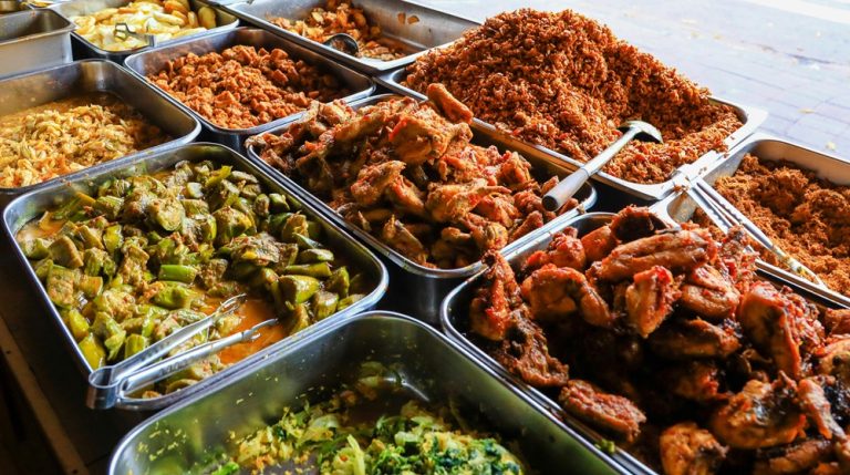 Food in Bali displayed at a traditional street food stall with rice dishes, vegetables, curries, grilled meats, and local specialties Caption Description