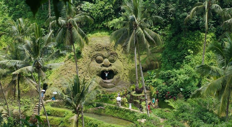 Ancient stone carving at Goa Gajah Temple surrounded by tropical vegetation in Bali Caption Description