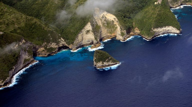 Aerial view of Kelingking Beach featured in this Nusa Penida travel guide, showing dramatic cliffs, turquoise water, and the iconic T-Rex-shaped headland Caption Description