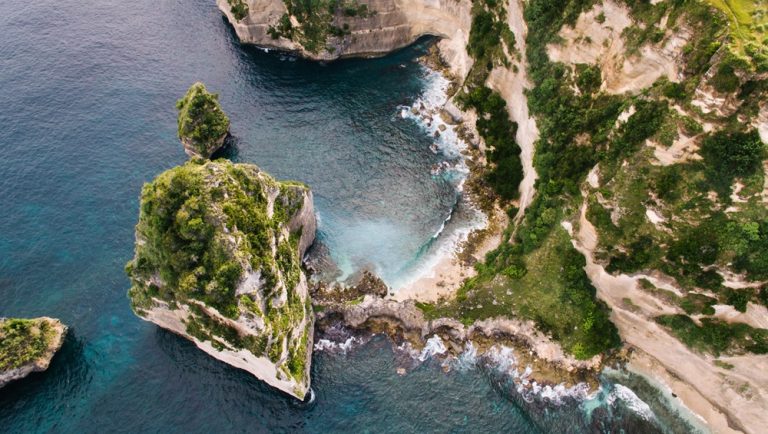 Aerial view of Kelingking Beach featured in this Nusa Penida travel guide, showing dramatic limestone cliffs and turquoise water below