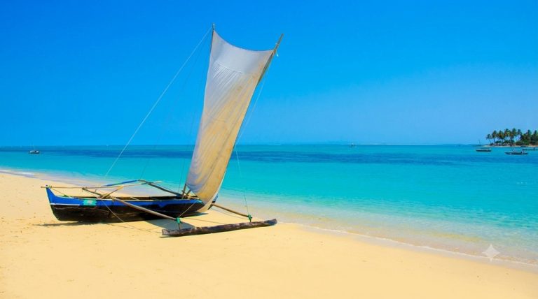 Pirogue à balancier traditionnelle malgache (lakana) amarrée sur le sable doré de la plage d'Anakao au sud de Tuléar, Madagascar, sous un ciel bleu clair et face à un lagon turquoise cristallin.