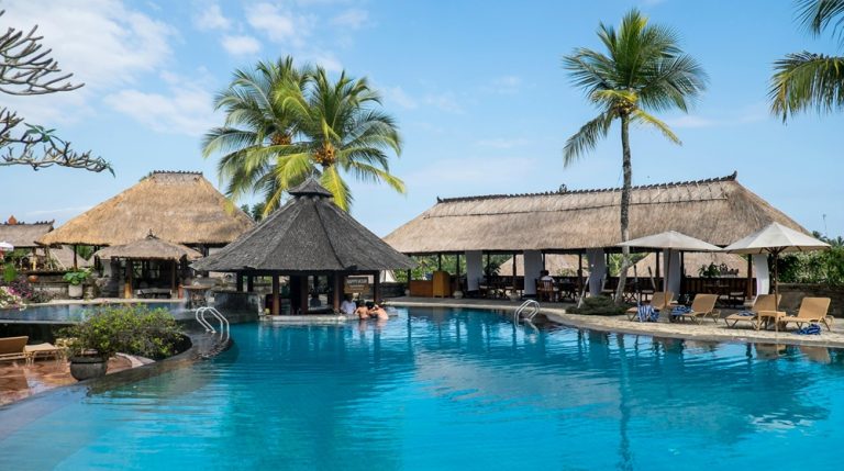 Luxury resort swimming pool surrounded by palm trees and traditional Balinese architecture in a tropical setting