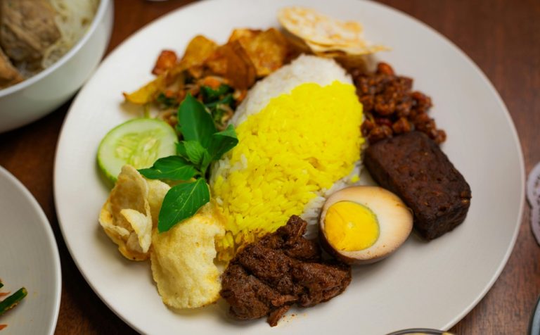 Food in Bali featuring Nasi Campur with rice, egg, spiced meat, vegetables, peanuts, crackers, and traditional Balinese side dishes Caption Description