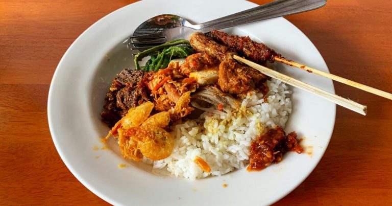 Food in Bali featuring Nasi Campur with rice, satay skewers, vegetables, sambal, egg, and traditional Balinese side dishes