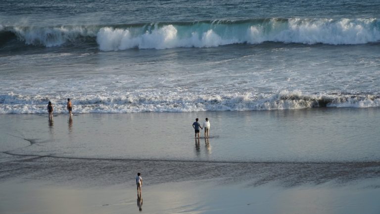 Seminyak travel guide featuring visitors walking along Seminyak Beach beside rolling ocean waves in Bali