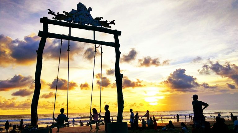 Visitors enjoying a beach swing at sunset along Seminyak Beach in Bali