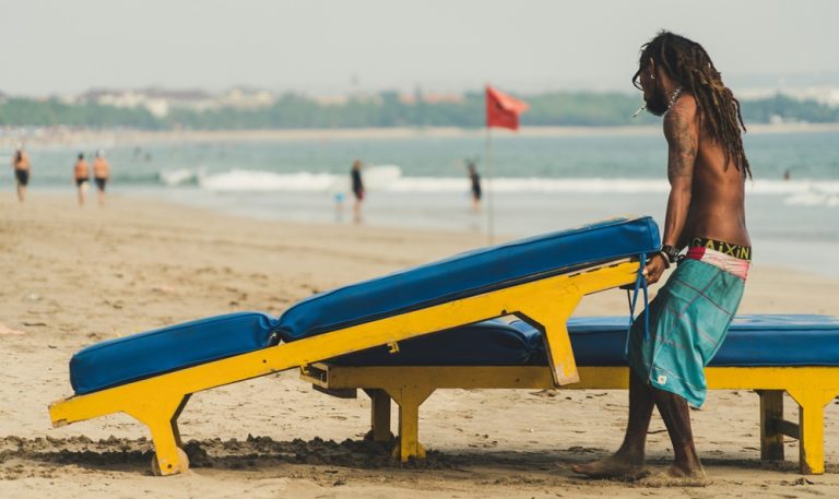 Local surfer preparing beach loungers along the shoreline in Seminyak, Bali Caption: Description: