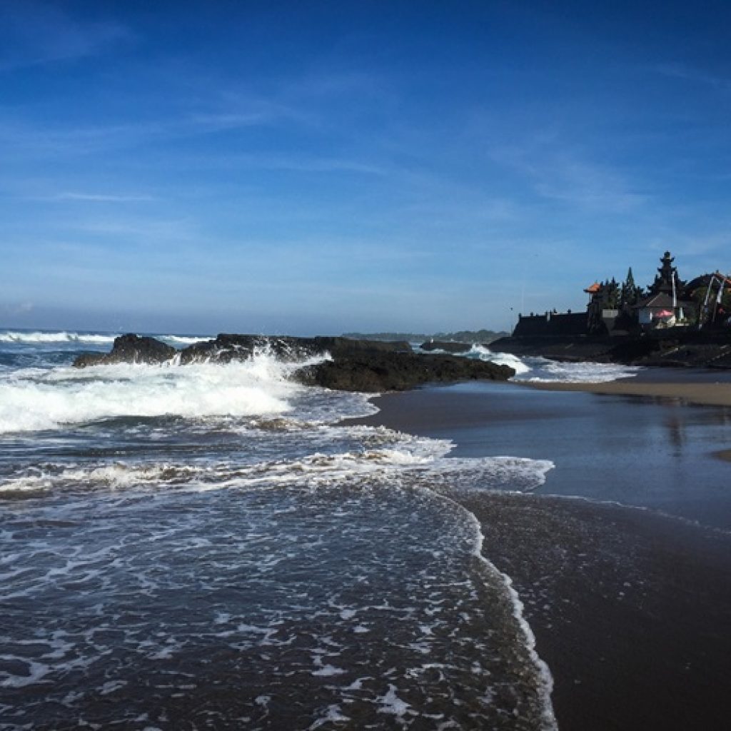 Canggu travel guide: Tanah Lot Temple coastline in Bali with waves crashing onto the beach and volcanic rocks near the famous sea temple