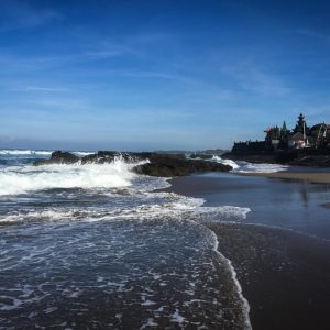Canggu travel guide: Tanah Lot Temple coastline in Bali with waves crashing onto the beach and volcanic rocks near the famous sea temple