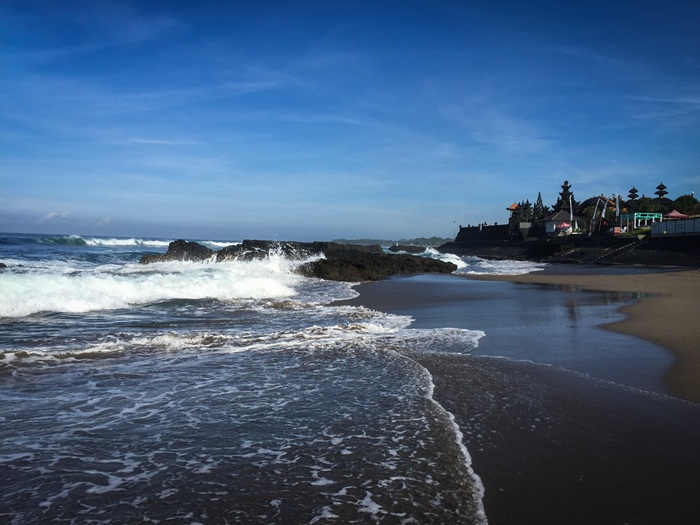 Canggu travel guide: Tanah Lot Temple coastline in Bali with waves crashing onto the beach and volcanic rocks near the famous sea temple