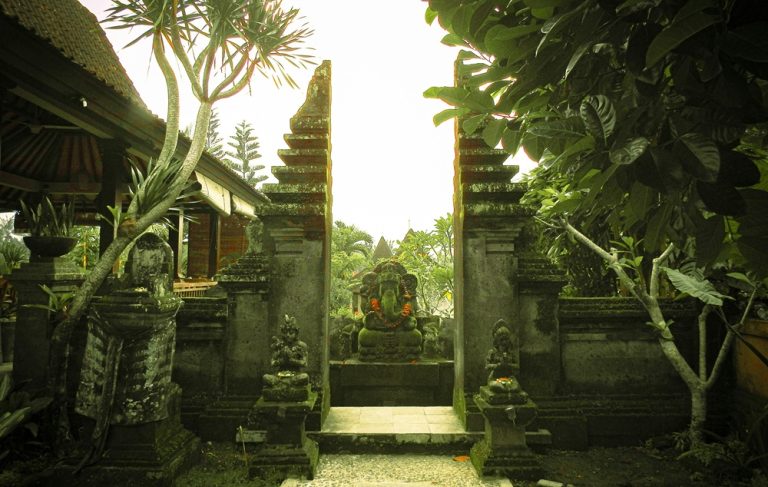 Traditional Balinese temple entrance surrounded by tropical gardens and stone carvings Caption Description