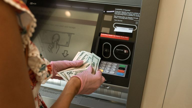 Traveler withdrawing cash from an ATM, illustrating ATM travel scams around the world and how to avoid card skimming and tourist fraud. Caption Description
