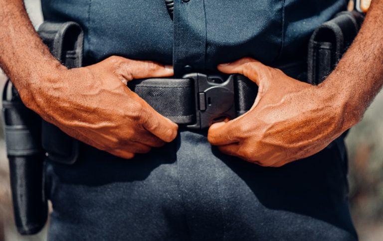 Person wearing a police uniform securing a duty belt, illustrating fake police travel scams around the world targeting unsuspecting tourists.