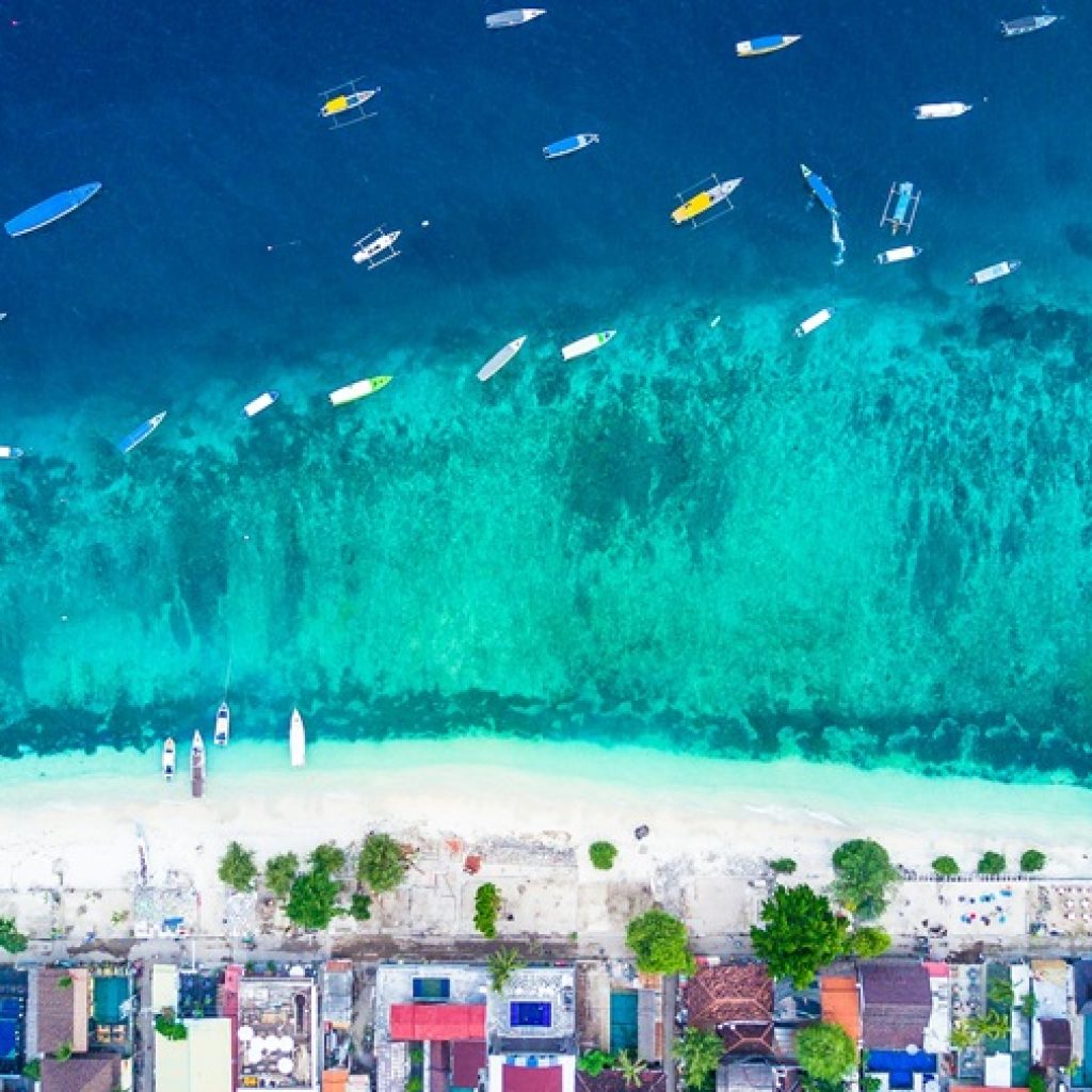 Aerial view of Gili Trawangan featured in this Gili Islands travel guide, showing turquoise water, white-sand beaches and boats anchored along the coastline.